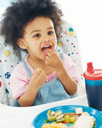 Fotografía de un niño pequeño comiendo sin ayuda en su silla alta para niños