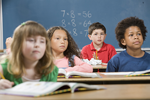 Children sitting at desks with books in classroom.