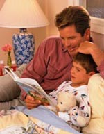 Imagen de un padre escuchando a su hijo leer un libro antes de acostarse