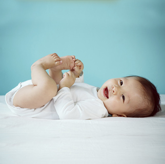 1 to 3 month old baby playing with feet while laying on her back.