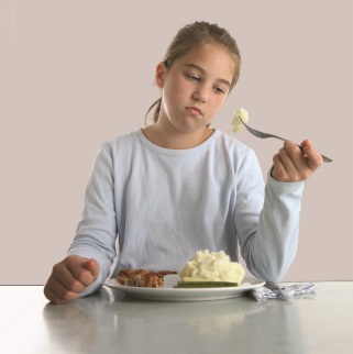 Young teen at dinner table, looking at forkful of mashed potatoes