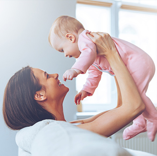 Mother holding her 4 to 6 month old in the air in a playful manor.