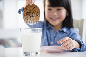 Girl dunking cookie in milk.