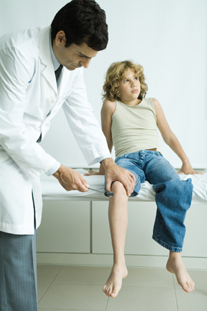 Male healthcare provider checking boy's reflexes.