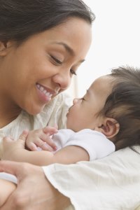 Primer plano de una mamá sonriendo y mirando a un bebé que duerme en sus brazos