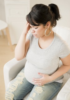 Pregnant woman with hand to head, eyes closed