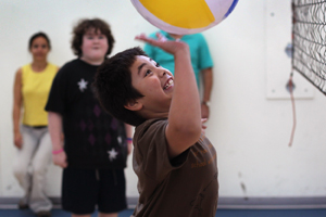 Boy hitting a beach ball in an indoor gym.