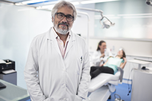 Male dentist standing and smiling in front of an exam chair.