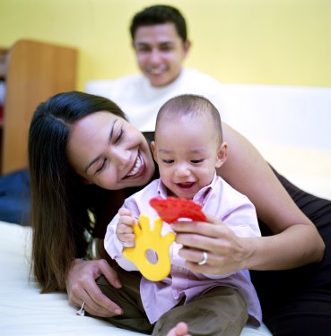 Mamá y papá con su bebé en la cama, jugando con objetos