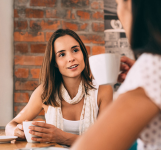 Two younger women talking over mugs of coffee