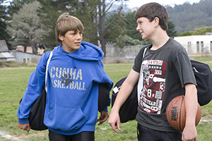 Two teen boys with sports gear talking outside.