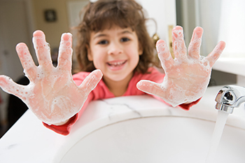 Una niña en un fregadero que muestra sus manos jabonosas