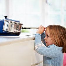 young child next to stove, hands on pot